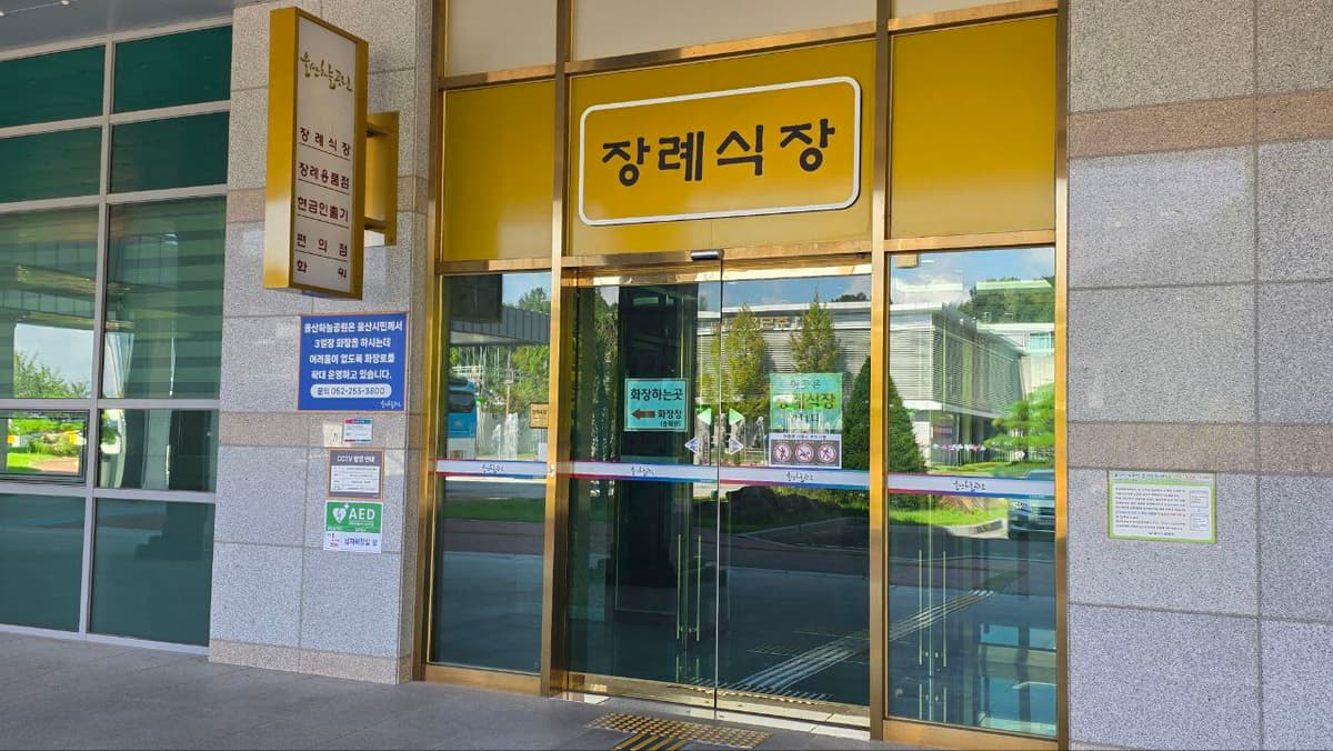 울산하늘공원장례식장 정문 출입구와 위치 안내 표지 유리문과 노란색 장례식장 표지판이 보임